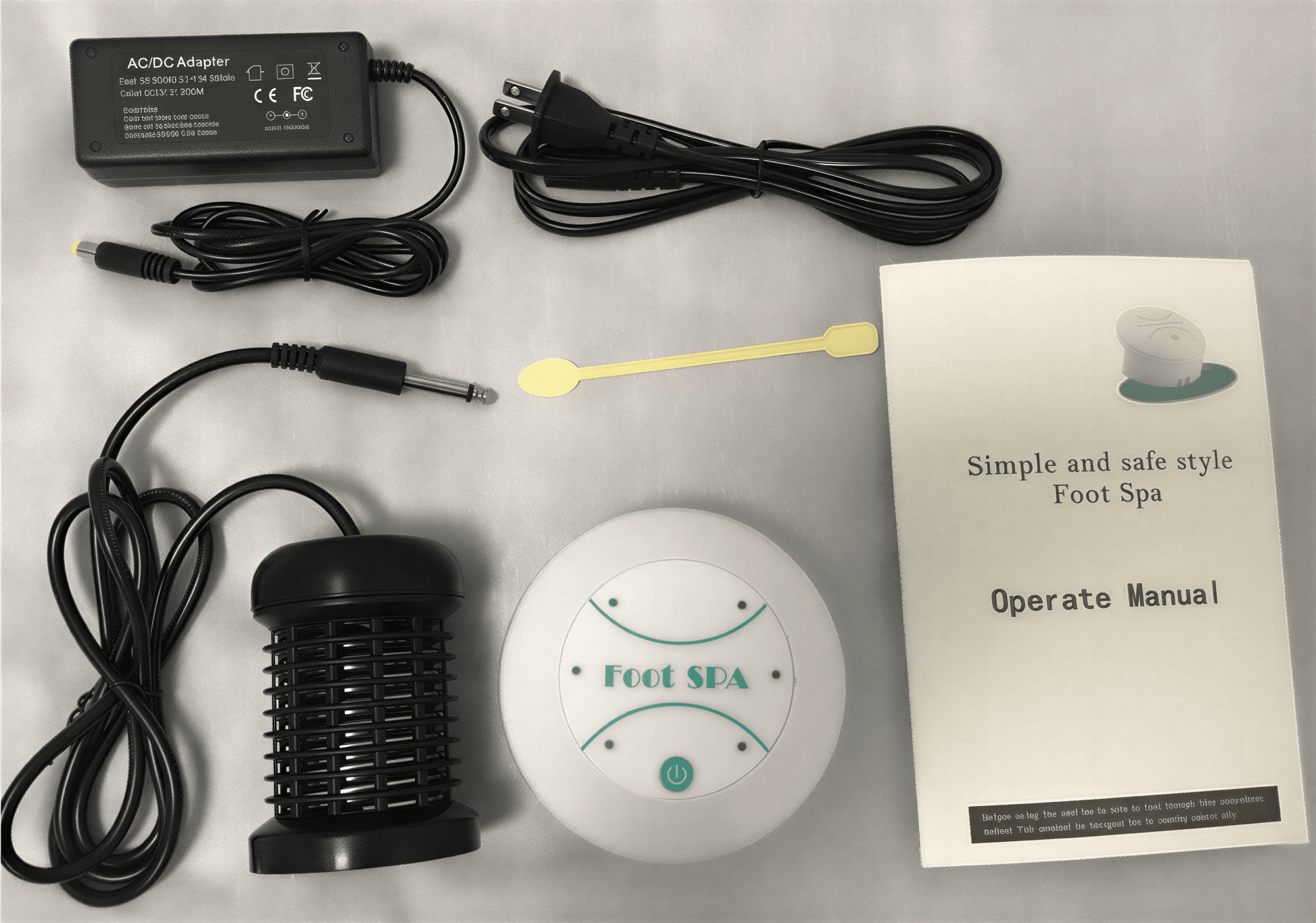 Mini foot massager with power adapter, foot spa device, manual, and cleaning tool arranged on a flat surface.